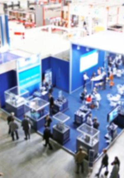 Fiera con stand blu, visitatori e prodotti esposti.