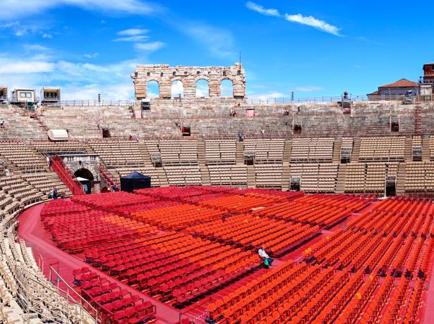 Antico anfiteatro con sedute rosse e beige, cielo sereno.