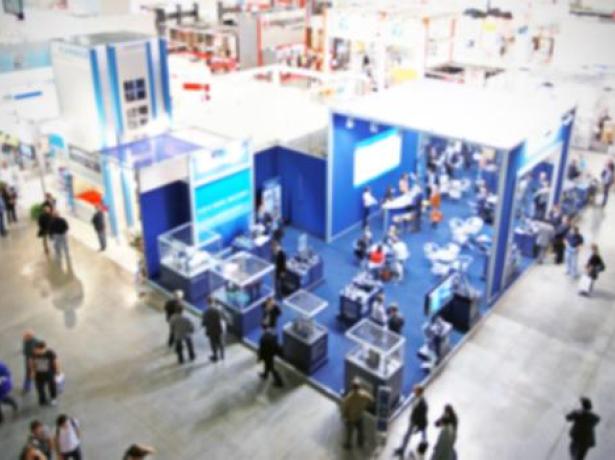 Fiera con stand blu, visitatori e prodotti esposti.