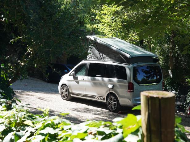 Camper in campeggio, tetto aperto, circondato da alberi.