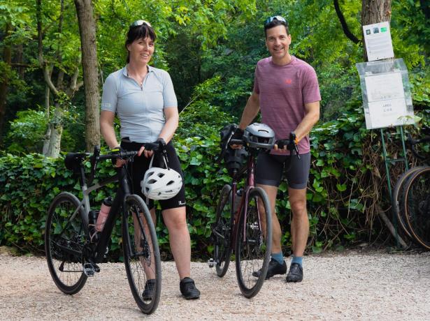 Deux cyclistes souriants avec des vélos dans un cadre verdoyant.